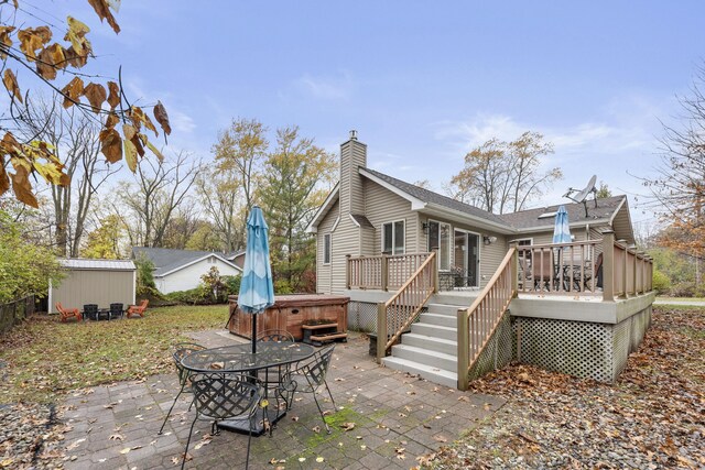 rear view of property featuring a wooden deck, a patio area, a shed, and a hot tub