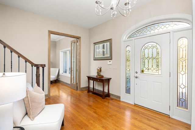 foyer entrance with ornamental molding, an inviting chandelier, and light wood-type flooring