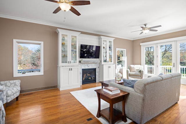 living room featuring ceiling fan, ornamental molding, light hardwood / wood-style flooring, and a fireplace