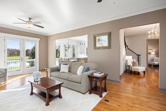 living room with french doors, ornamental molding, ceiling fan with notable chandelier, and light wood-type flooring