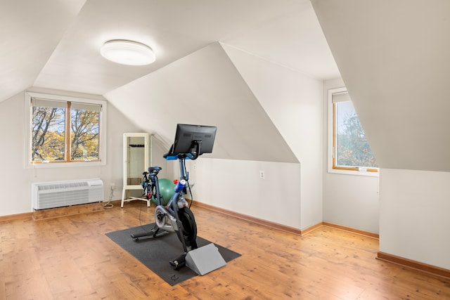 exercise room with an AC wall unit, vaulted ceiling, and light wood-type flooring