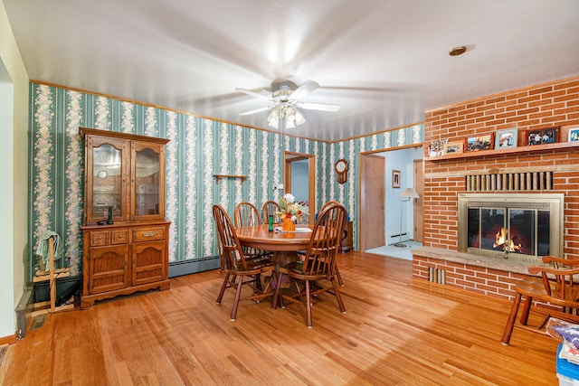 dining space with a baseboard radiator, hardwood / wood-style flooring, a fireplace, and ceiling fan