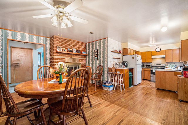 dining space with a brick fireplace, light hardwood / wood-style floors, and ceiling fan