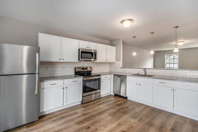 kitchen with appliances with stainless steel finishes, sink, pendant lighting, and white cabinets