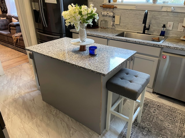 kitchen featuring tasteful backsplash, sink, dishwasher, a center island, and black fridge