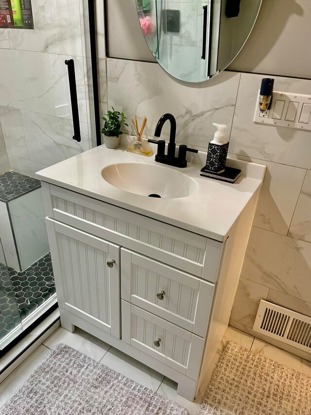 bathroom featuring tasteful backsplash, a shower with door, tile walls, vanity, and tile patterned flooring