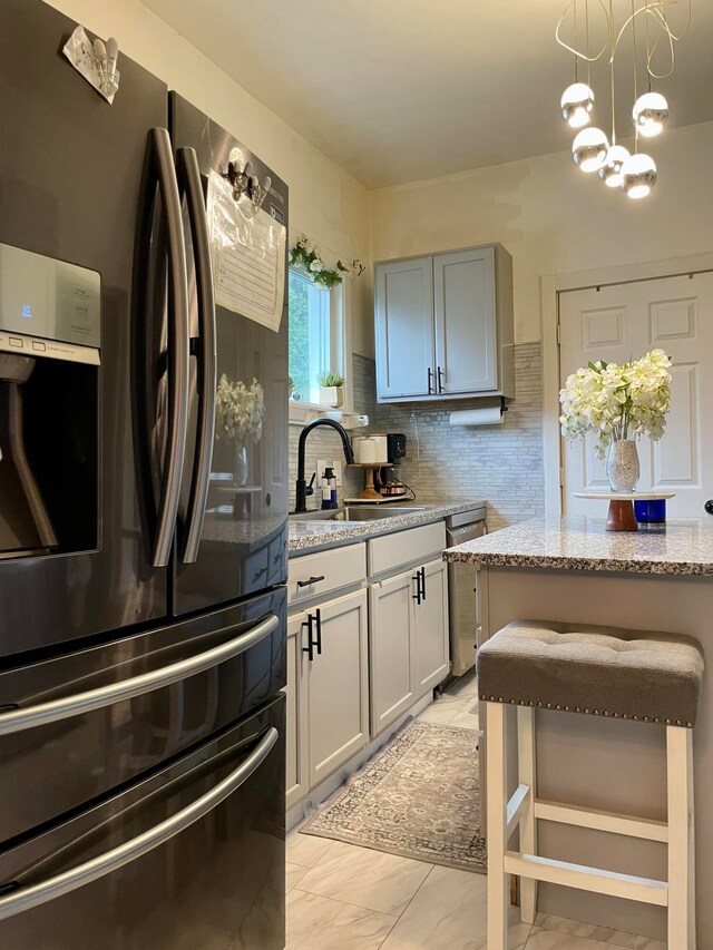 kitchen featuring tasteful backsplash, sink, stainless steel appliances, light stone counters, and a chandelier