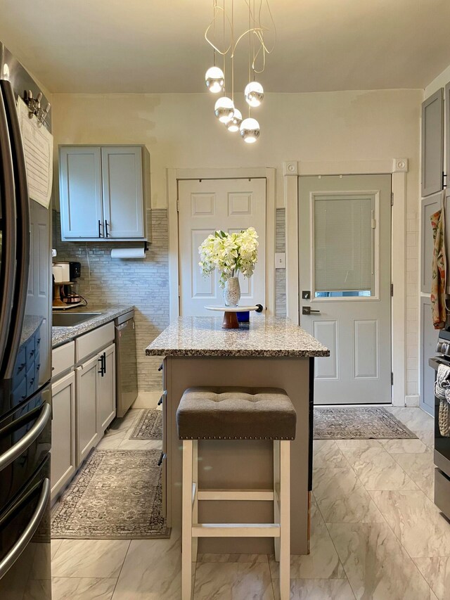 kitchen with decorative backsplash, appliances with stainless steel finishes, light stone countertops, gray cabinets, and a notable chandelier