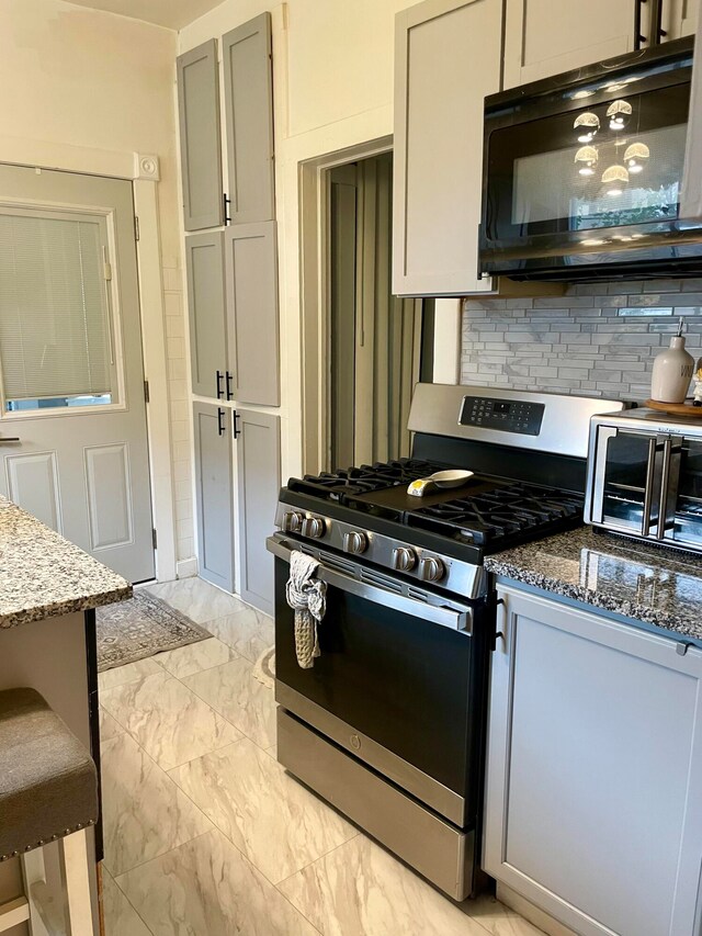 kitchen featuring stone countertops, gas stove, tasteful backsplash, and gray cabinets