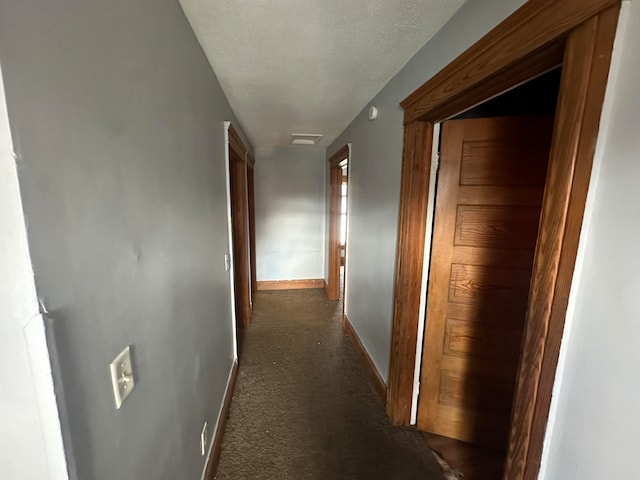 hallway featuring dark colored carpet and a textured ceiling