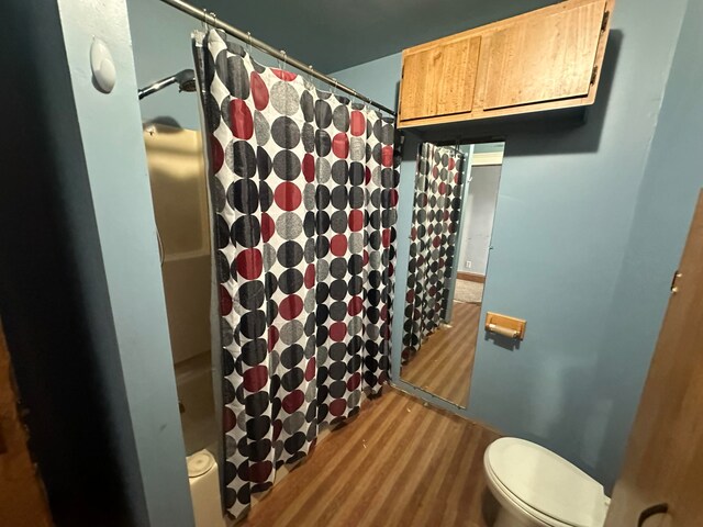 bathroom with hardwood / wood-style floors, a shower with shower curtain, and toilet