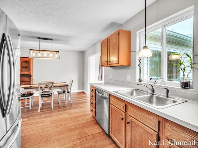 kitchen with appliances with stainless steel finishes, a textured ceiling, sink, decorative light fixtures, and light hardwood / wood-style floors