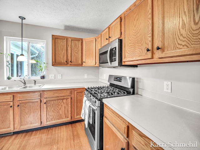 kitchen with pendant lighting, sink, a textured ceiling, light hardwood / wood-style floors, and stainless steel appliances