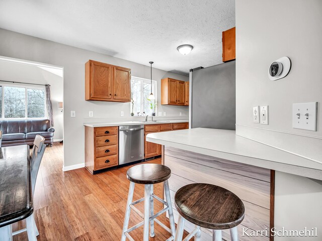 kitchen with sink, stainless steel dishwasher, a textured ceiling, decorative light fixtures, and a breakfast bar area