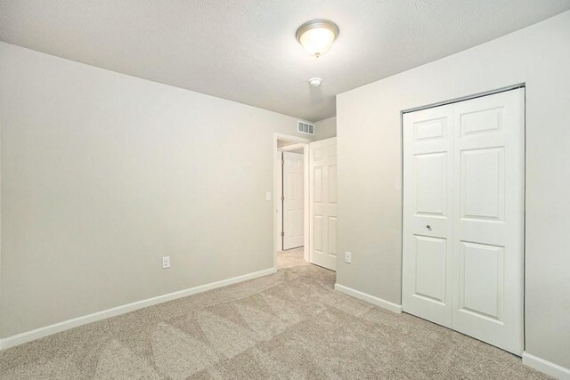 unfurnished bedroom featuring a closet, a textured ceiling, and light colored carpet