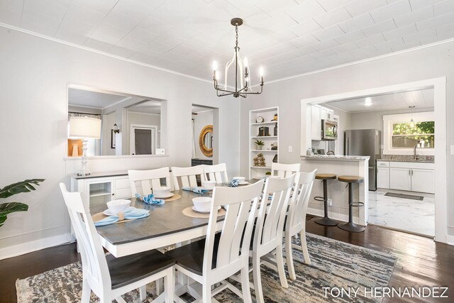 dining room featuring dark wood-type flooring, sink, built in shelves, ornamental molding, and a notable chandelier