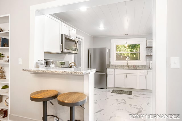 kitchen featuring light stone countertops, appliances with stainless steel finishes, a kitchen breakfast bar, sink, and white cabinets