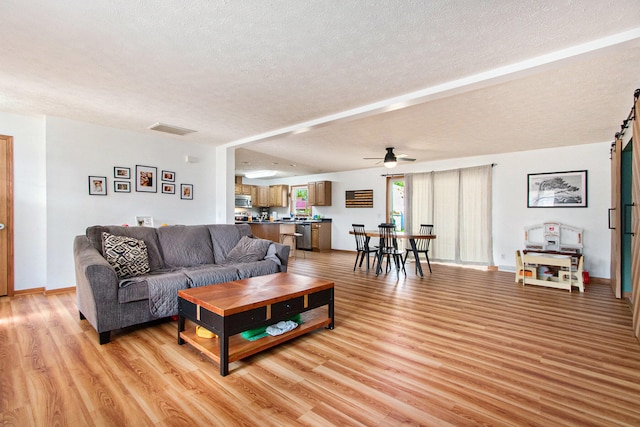 living room with ceiling fan, a textured ceiling, and light wood-type flooring