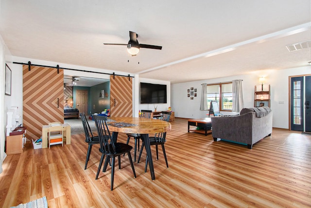 dining area with light hardwood / wood-style floors, a textured ceiling, a barn door, and ceiling fan