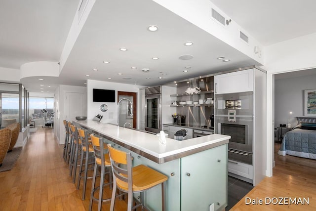 kitchen with oven, kitchen peninsula, white cabinets, a breakfast bar, and hardwood / wood-style flooring