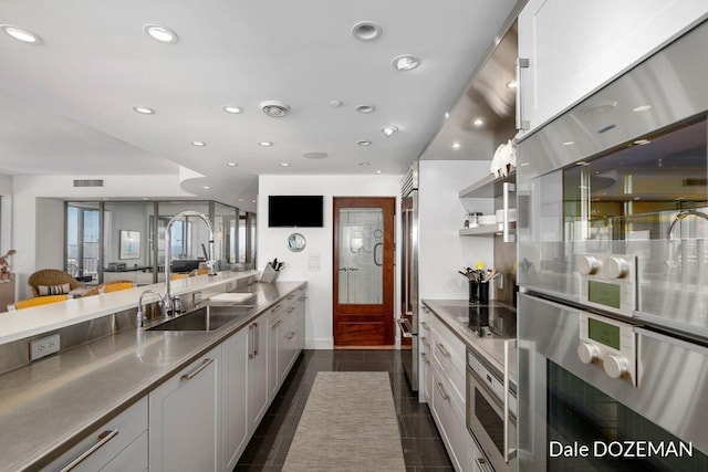 kitchen with black electric stovetop, stainless steel double oven, stainless steel counters, sink, and white cabinetry