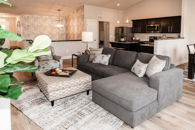 living room with high vaulted ceiling, an inviting chandelier, and light wood-type flooring