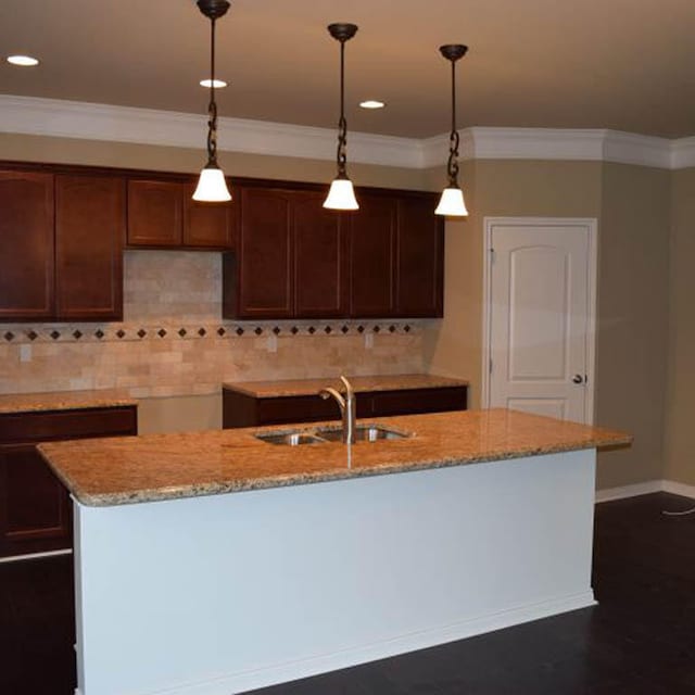 kitchen with hanging light fixtures, sink, light stone counters, and decorative backsplash