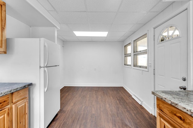 kitchen with a drop ceiling, white fridge, light stone counters, and dark wood-type flooring