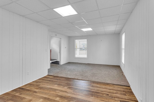 empty room featuring a drop ceiling, wooden walls, and wood-type flooring