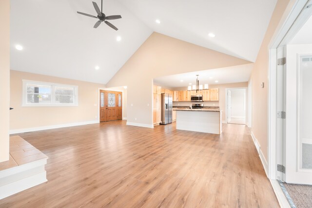 unfurnished living room with high vaulted ceiling, light hardwood / wood-style floors, and ceiling fan with notable chandelier