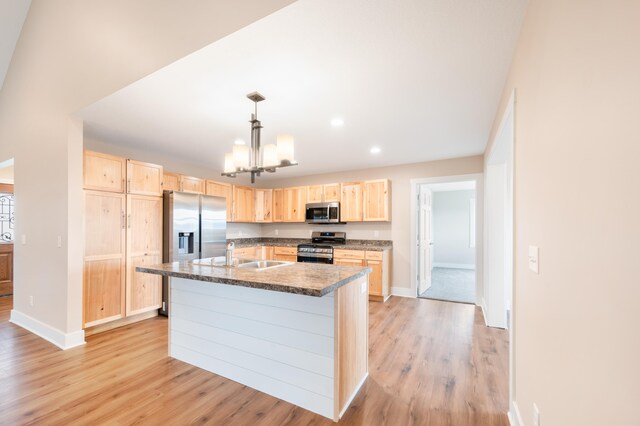 kitchen with stainless steel appliances, pendant lighting, light brown cabinets, an island with sink, and light hardwood / wood-style floors