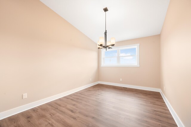 spare room featuring wood-type flooring, vaulted ceiling, and a notable chandelier