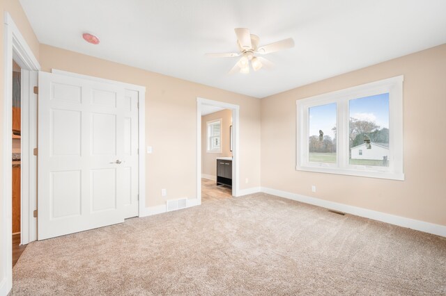 unfurnished bedroom featuring light colored carpet, ceiling fan, and ensuite bath