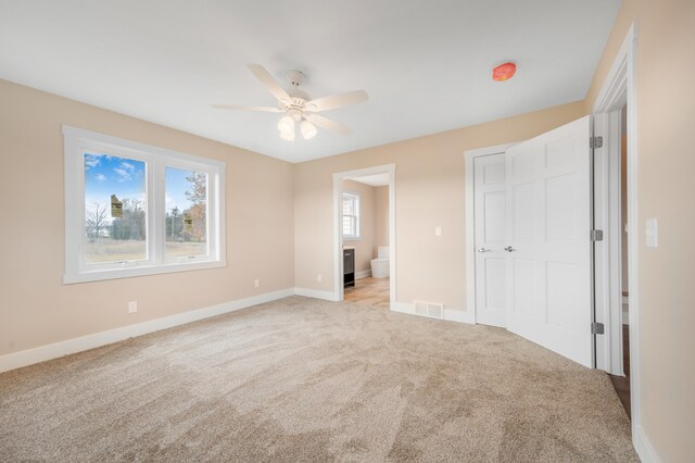 unfurnished bedroom with light colored carpet, ceiling fan, and ensuite bath