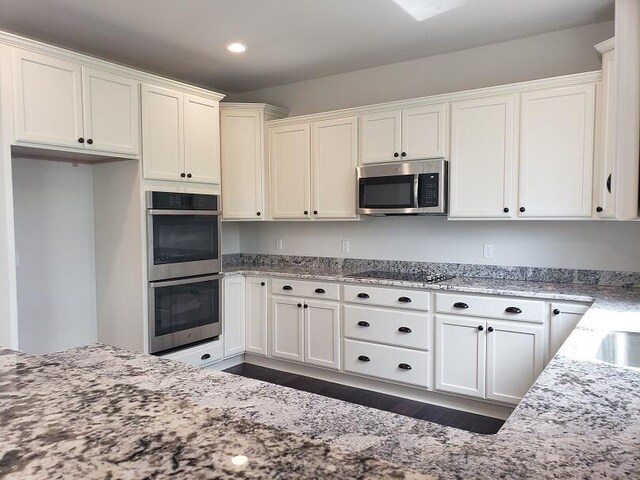 kitchen featuring dark wood-type flooring, white cabinetry, light stone counters, and stainless steel appliances