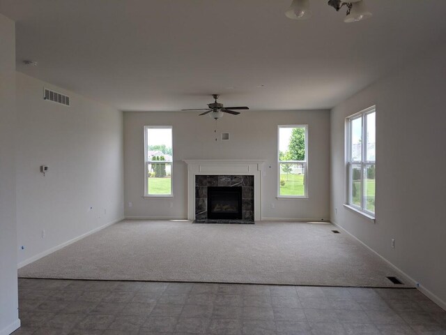 unfurnished living room featuring ceiling fan, light colored carpet, a tile fireplace, and plenty of natural light