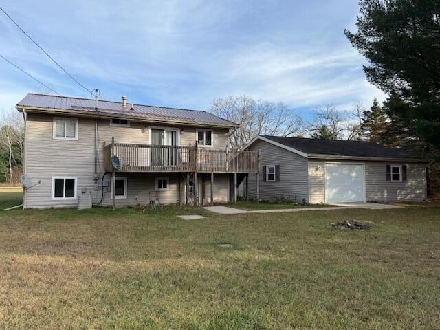 rear view of house featuring an outdoor structure, a wooden deck, a garage, and a lawn