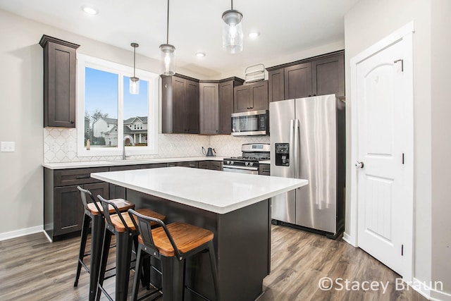 kitchen featuring sink, appliances with stainless steel finishes, hanging light fixtures, a kitchen island, and dark wood-type flooring