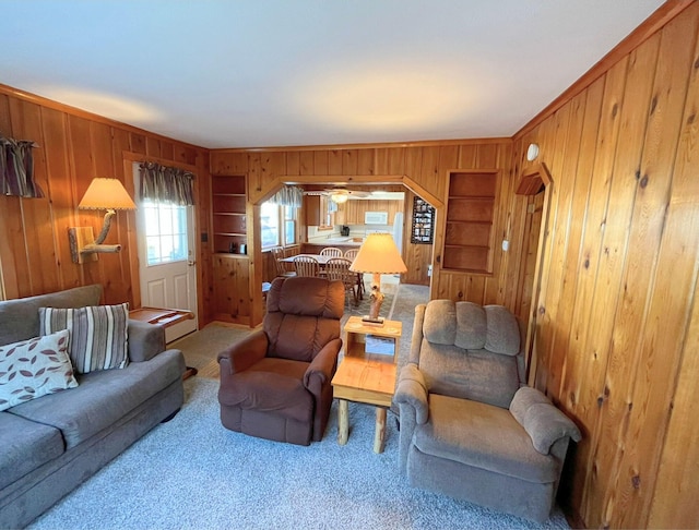 living room with crown molding, wooden walls, carpet, and ceiling fan