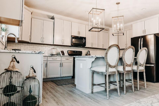 kitchen featuring appliances with stainless steel finishes, light hardwood / wood-style floors, decorative light fixtures, white cabinets, and ornamental molding