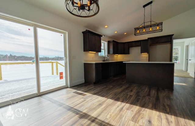 kitchen with lofted ceiling, sink, dark brown cabinets, wood-type flooring, and a kitchen island