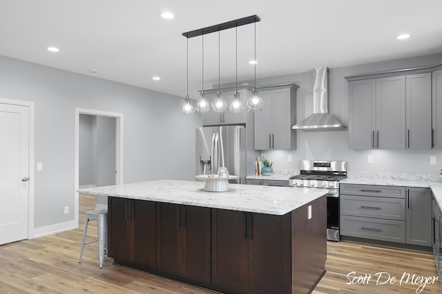 kitchen featuring a kitchen island, appliances with stainless steel finishes, a breakfast bar, wall chimney exhaust hood, and light hardwood / wood-style flooring