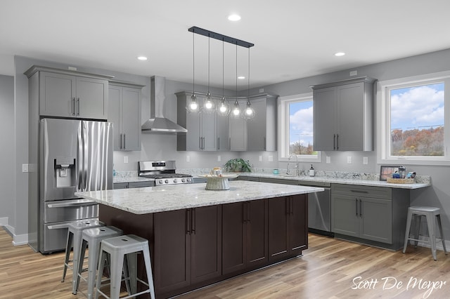 kitchen with stainless steel appliances, pendant lighting, a wealth of natural light, wall chimney exhaust hood, and a center island