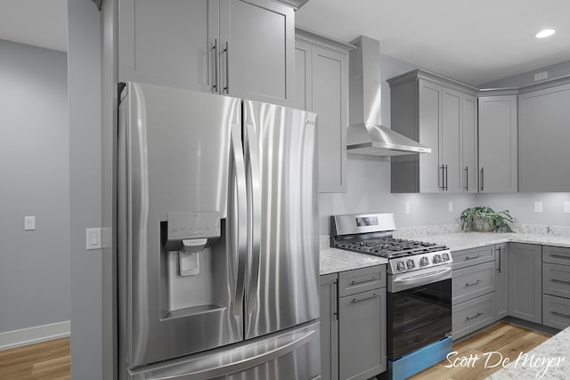 kitchen with light hardwood / wood-style flooring, light stone countertops, wall chimney exhaust hood, and stainless steel appliances