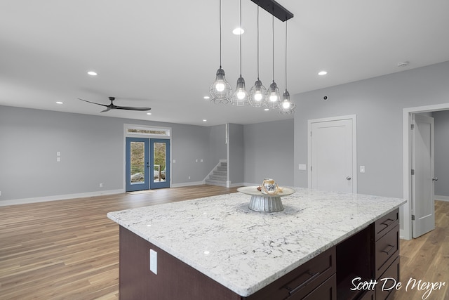 kitchen featuring hanging light fixtures, a kitchen island, light stone countertops, dark brown cabinets, and light hardwood / wood-style flooring