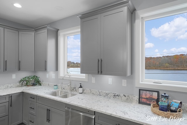 kitchen featuring gray cabinets, light stone countertops, sink, dishwasher, and a water view