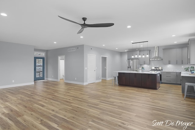 kitchen with light hardwood / wood-style floors, a center island, gray cabinetry, wall chimney range hood, and appliances with stainless steel finishes