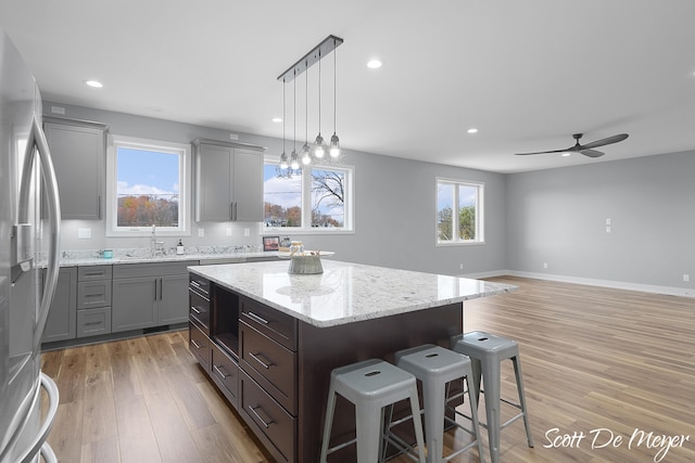 kitchen with ceiling fan with notable chandelier, a center island, sink, light hardwood / wood-style flooring, and stainless steel fridge