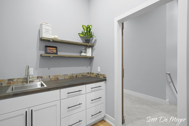 bar featuring white cabinetry, sink, and light carpet