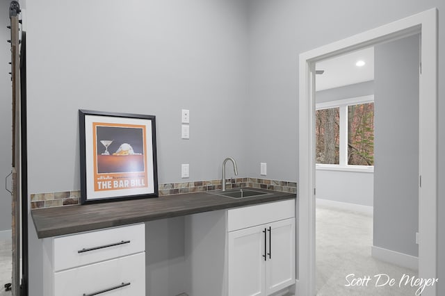 bar featuring light colored carpet, white cabinetry, and sink